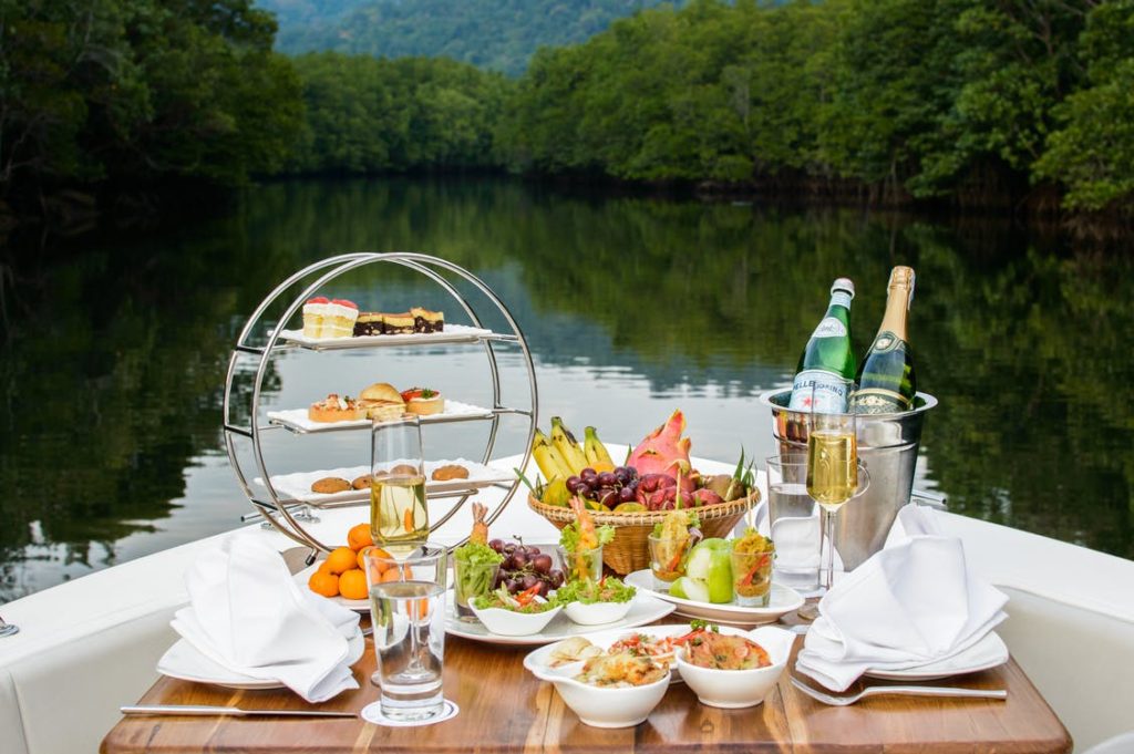 The Best Wines To Pair With Seafood 2 A table laid out on a boat with several wine varieties, fruits, desserts, and fish.